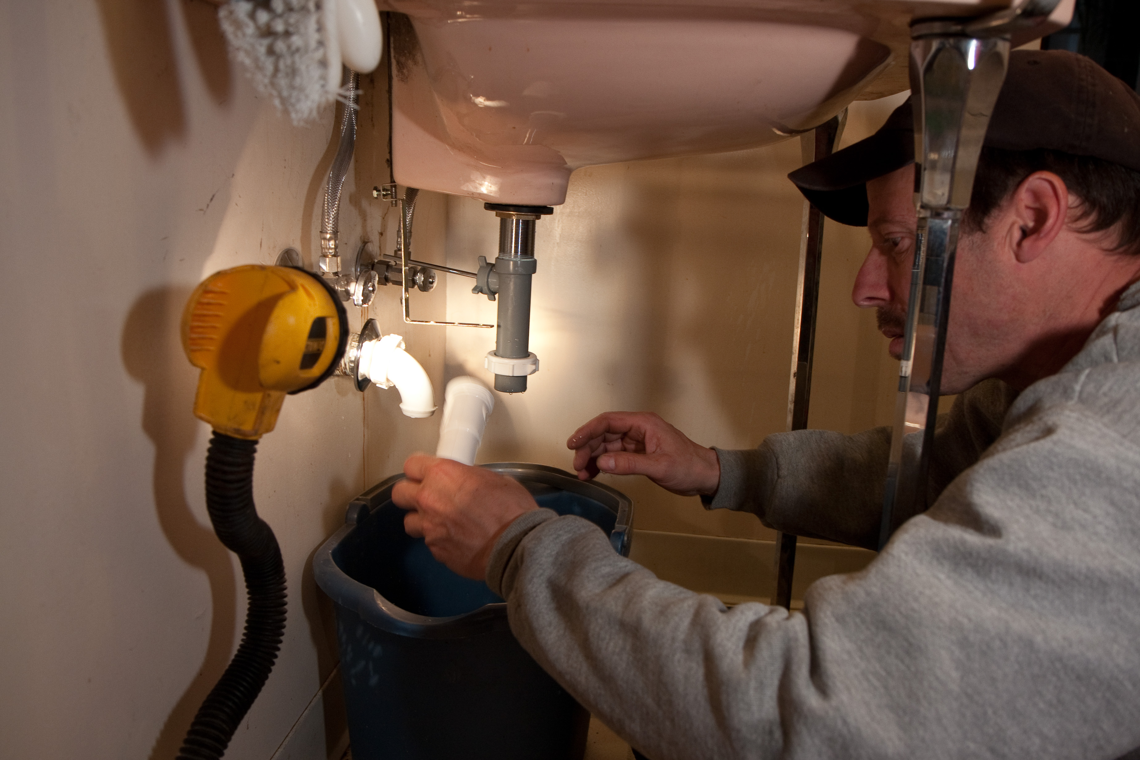A plumber repairing residential plumbing beneath a sink